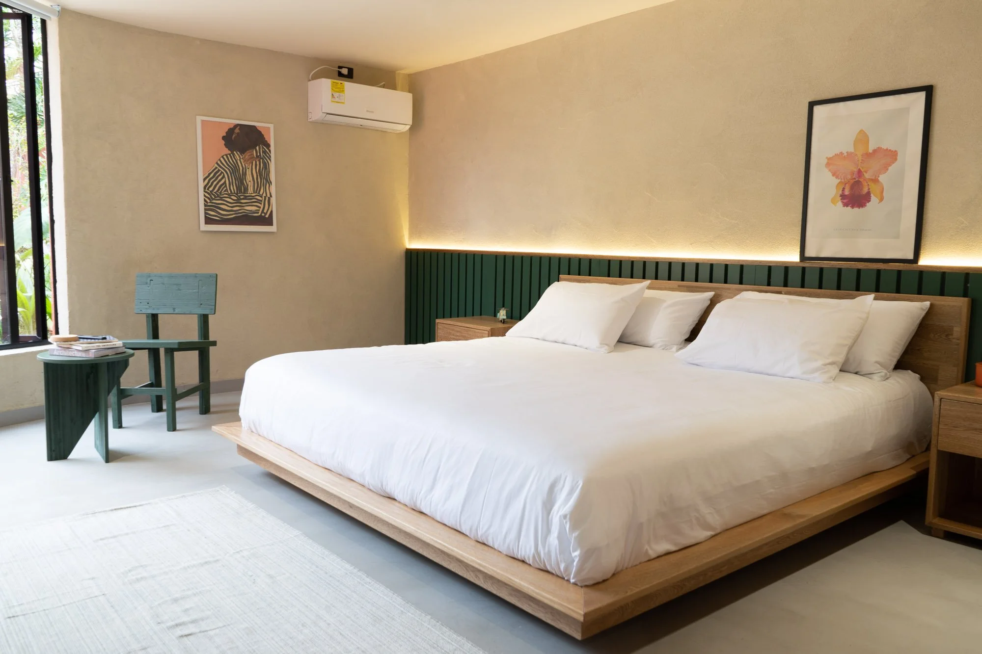 Habitación moderna con cama grande de sábanas blancas, arte en las paredes y aire acondicionado.