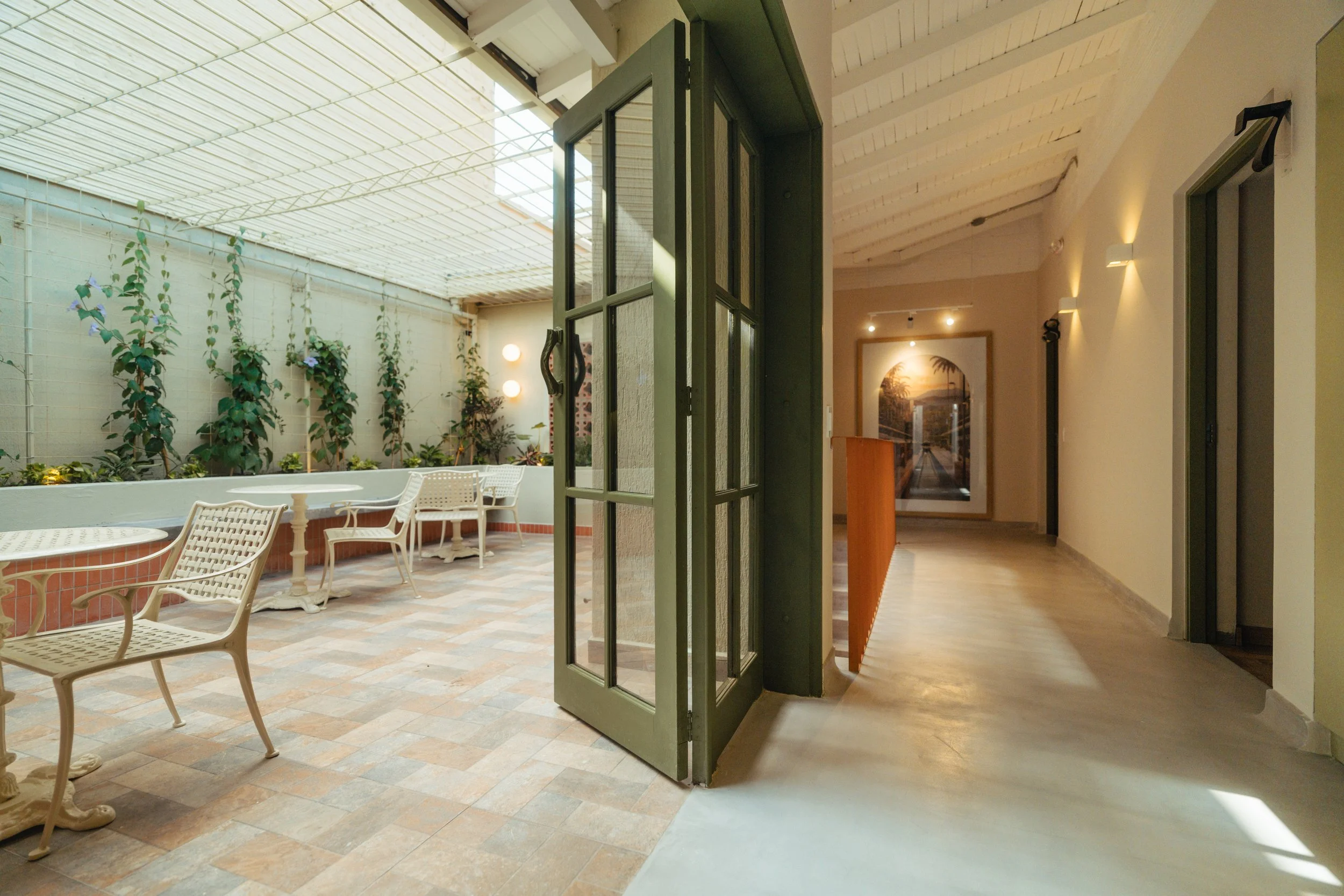 Interior de un espacio con área de descanso y plantas, con puertas de vidrio y paredes iluminadas.