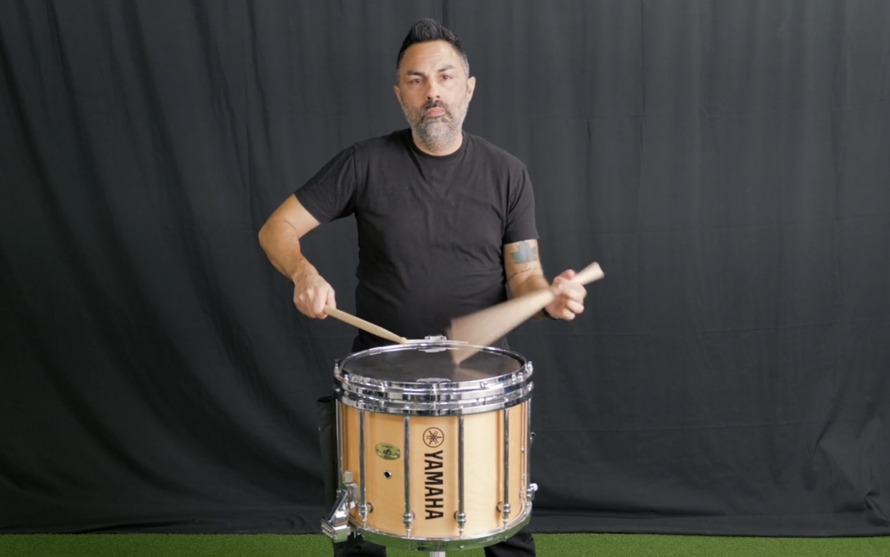 A person walking outdoors on a paved area, wearing black athletic shorts, gray running shoes, and white socks, with a nearby modern brick building and green land in the background. The image displays a heart rate of 112 BPM in the bottom right corner.