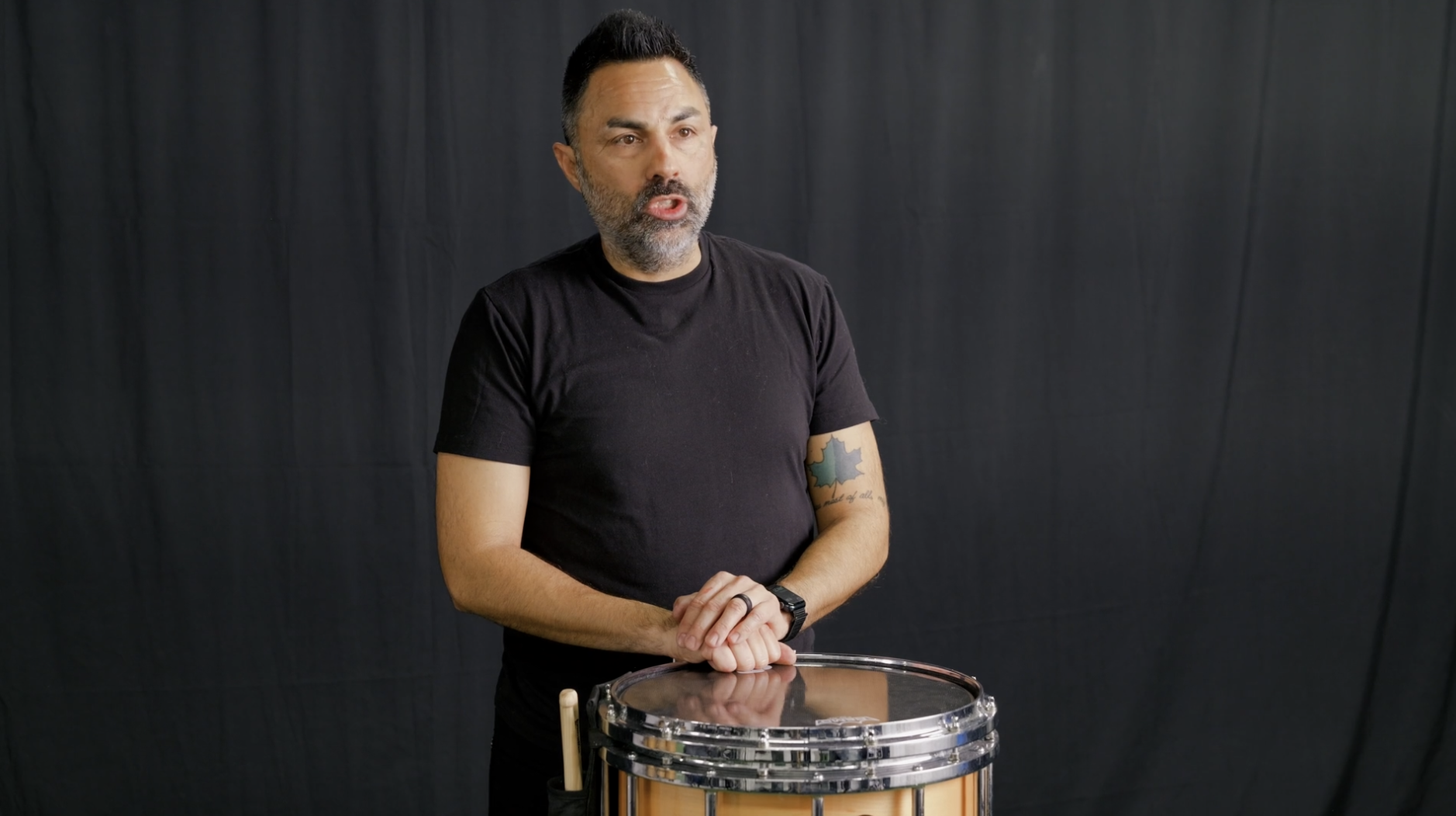A man in black sportswear and white sneakers standing on a green turf floor in front of a black backdrop, demonstrating a foot positioning tip for walking or running.