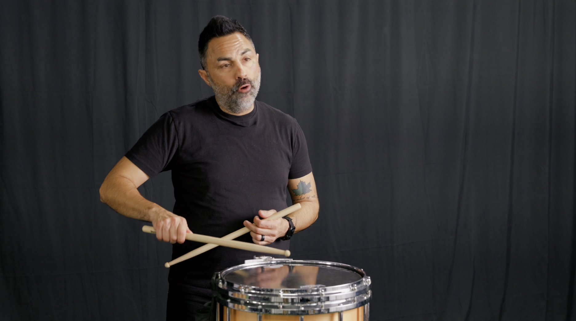 A man standing on a green artificial turf with arms raised and spread apart, against a black backdrop.