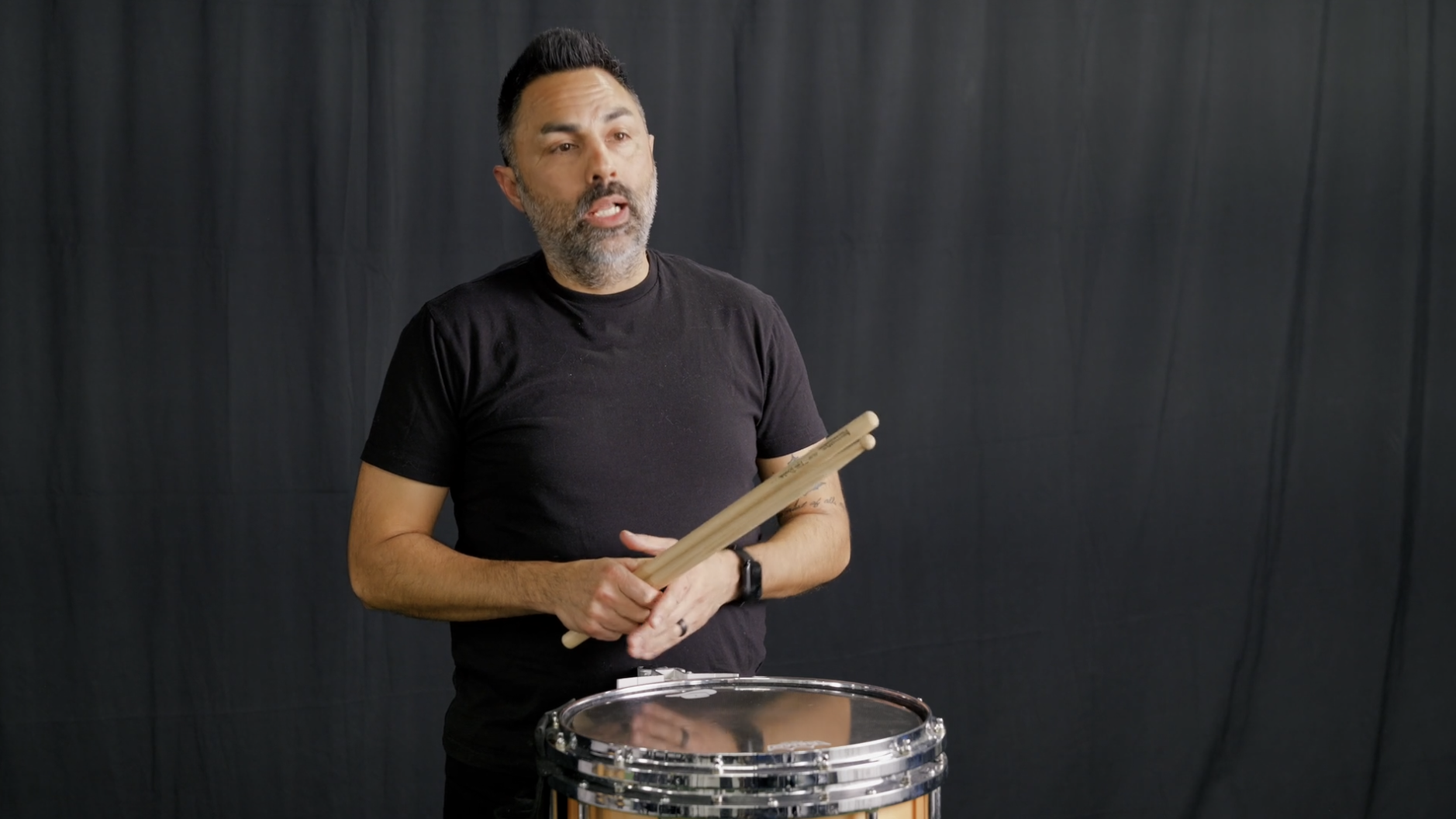A man dressed in black athletic wear, including a backwards baseball cap, walking on green turf against a black backdrop.