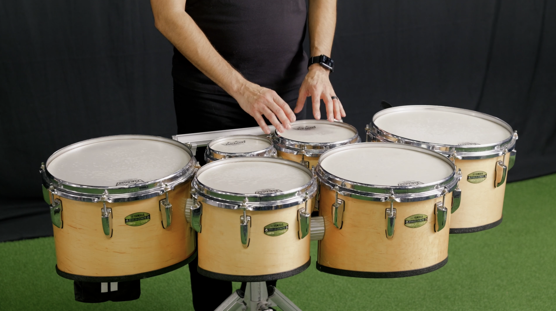 Man standing on green turf with black background, looking down, arms extended downward.