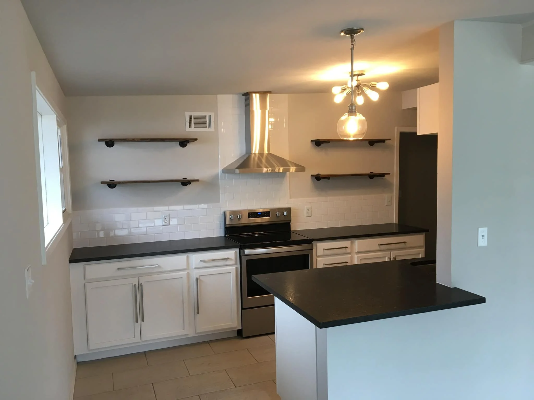 Modern kitchen with white cabinets, black countertops, stainless steel stove, and open wooden shelves on the wall.