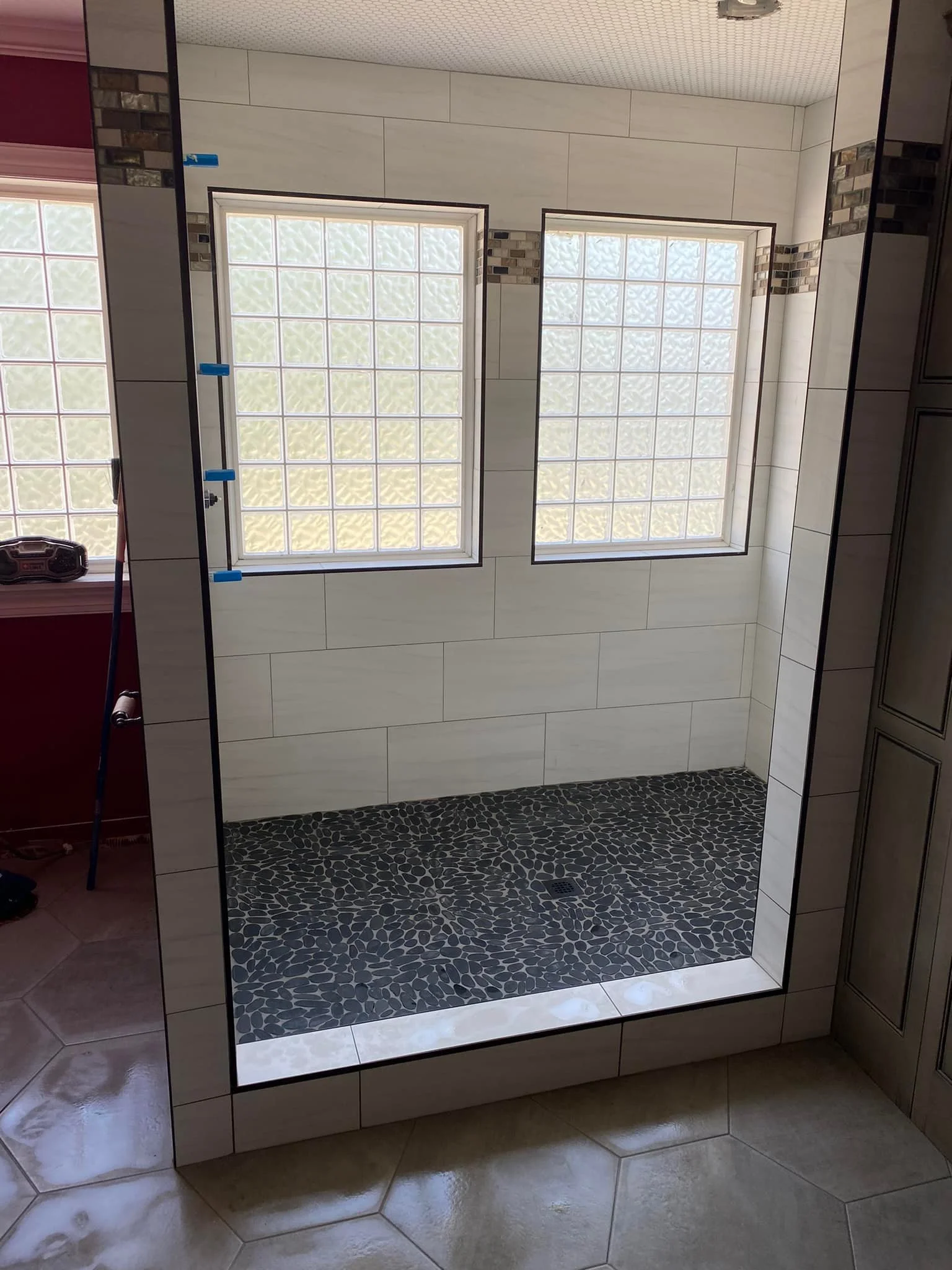 Bathroom shower with glass block windows, pebble stone floor, and tiled walls.