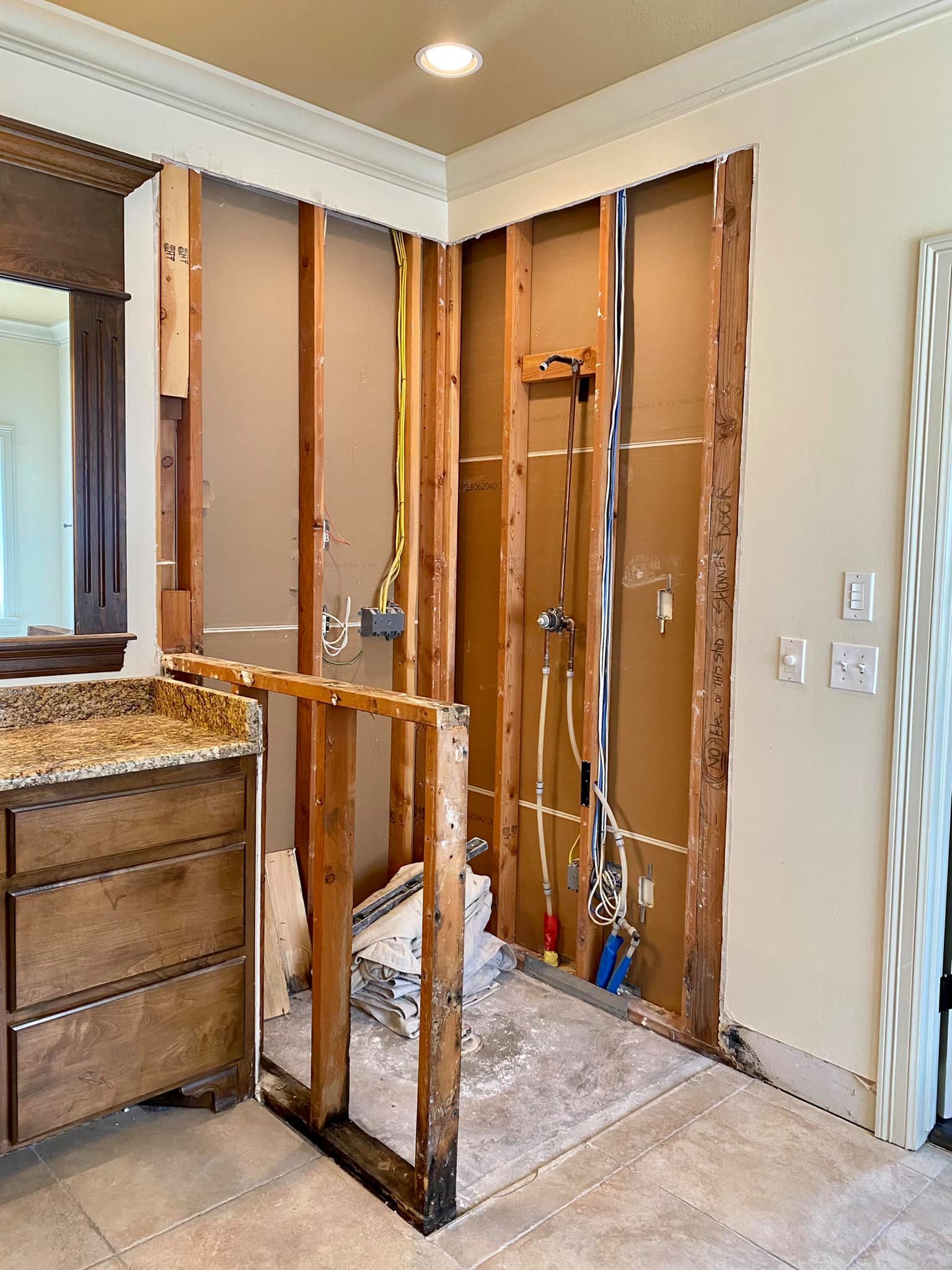 Kitchen area with exposed wall framing, electrical wiring, plumbing, and construction materials for renovation.