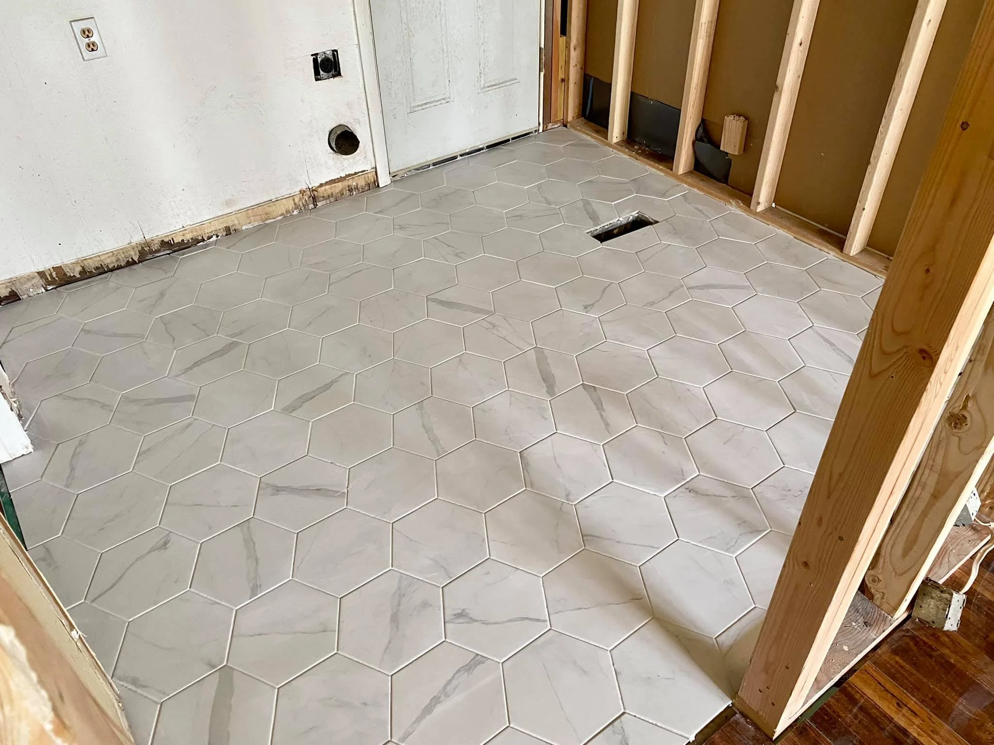 Part of a room under renovation with new hexagon-shaped tile flooring, exposed wall studs, electrical outlets, and unfinished walls.