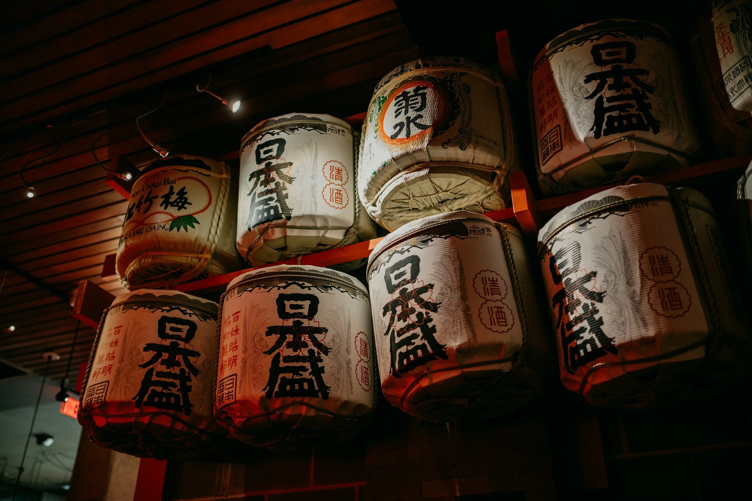 Japanese paper lanterns hanging from a wooden ceiling, decorated with Japanese characters and symbols.