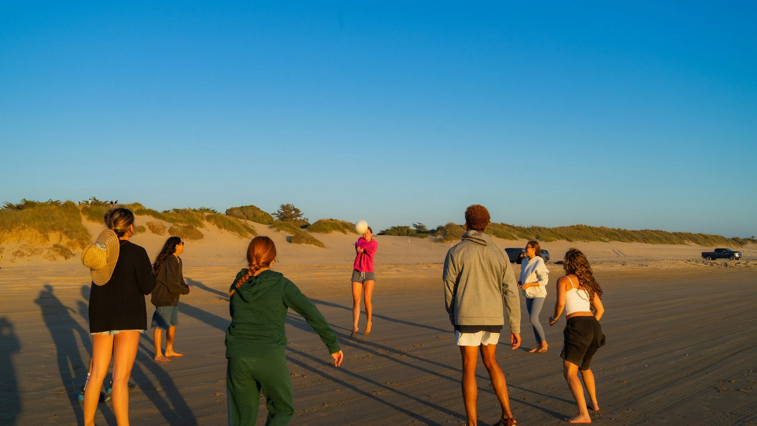 Group of people playing volleyball on a sandy beach during sunset