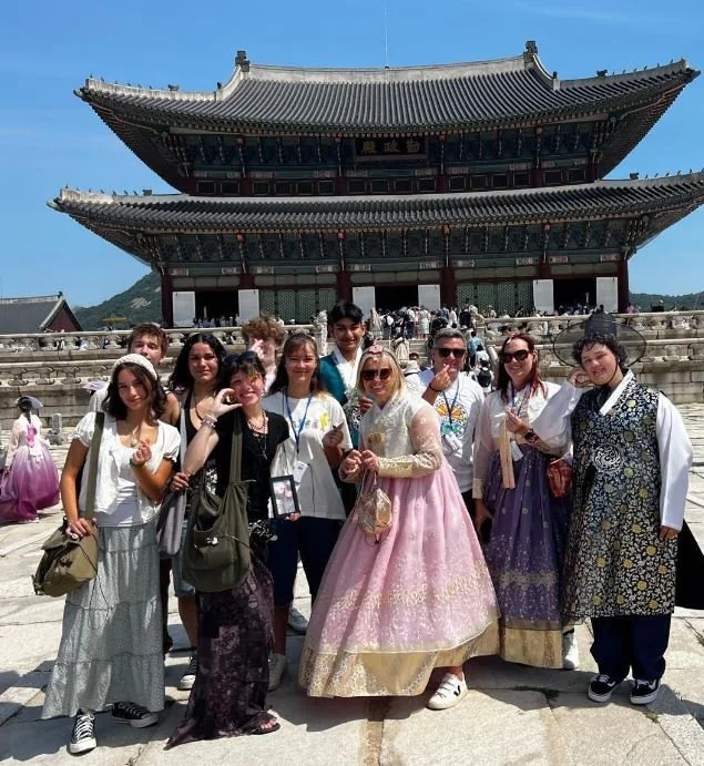 Group of tourists posing in front of a traditional Korean palace with a large, multi-tiered roof.