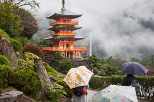 A traditional Japanese pagoda in a misty garden with visitors holding umbrellas.