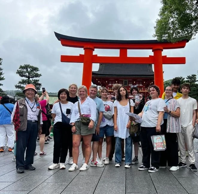 Group of tourists standing in front of a large red torii gate at a traditional Japanese shrine.