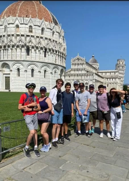 Group of young tourists posing in front of the Leaning Tower of Pisa in Italy.