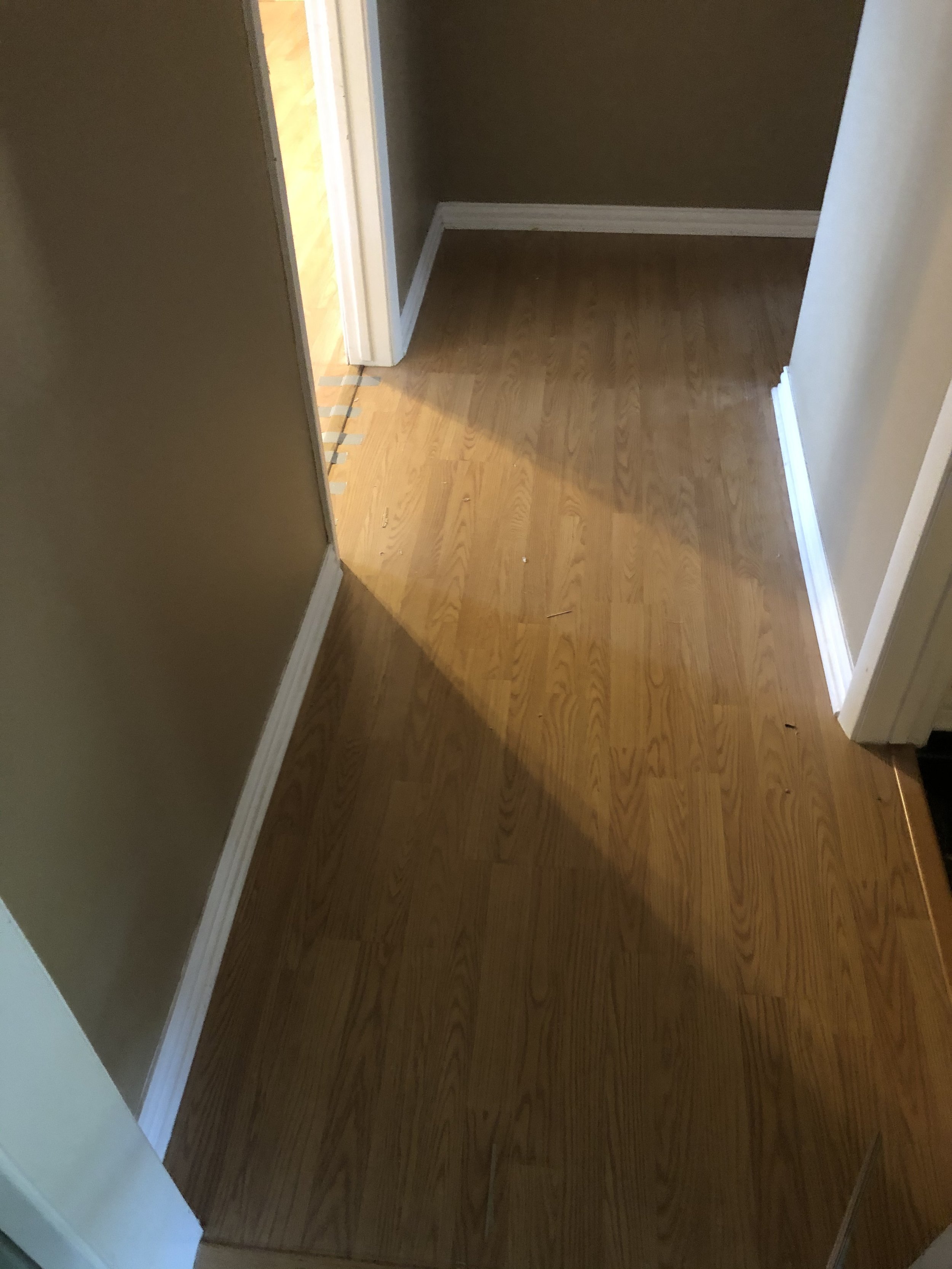 Narrow hallway with brown wood flooring and white baseboards.