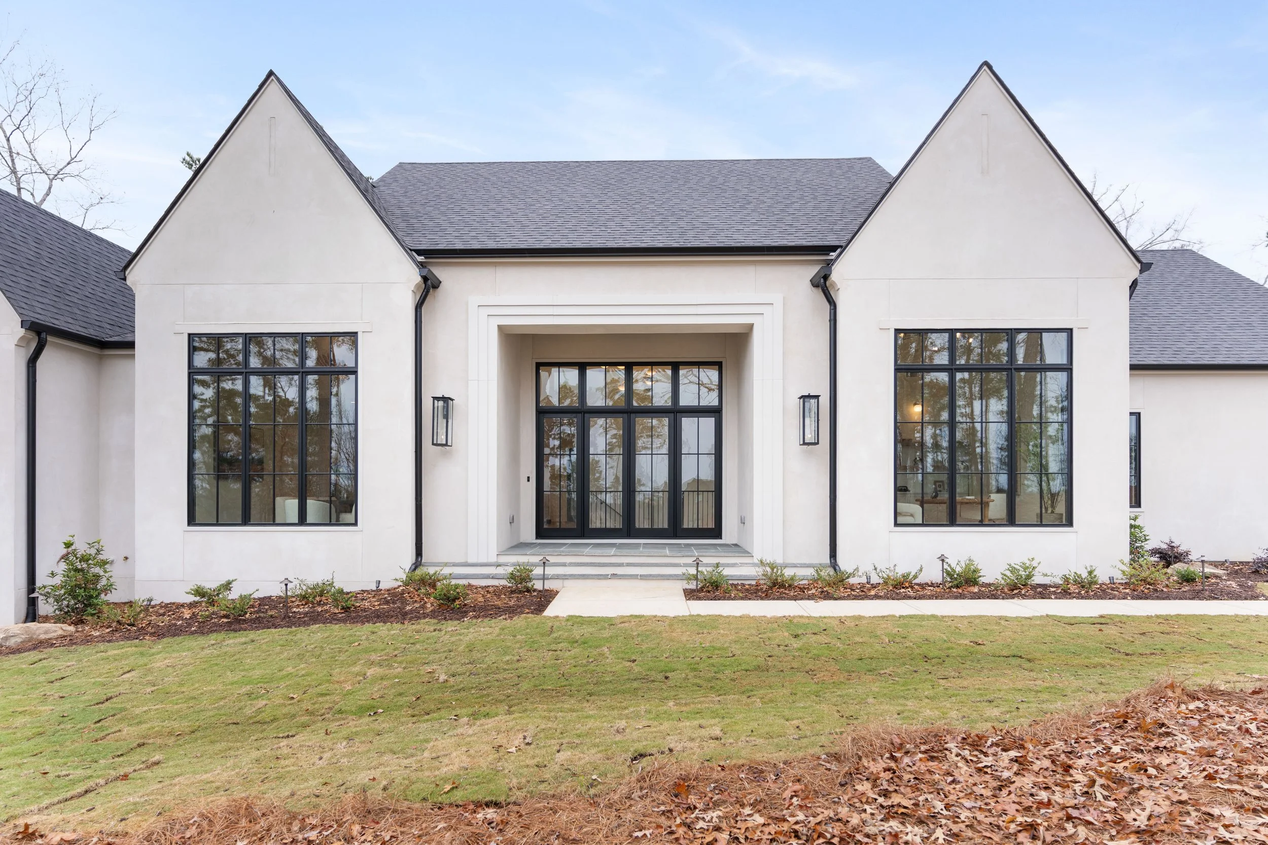 Front view of a modern house with large windows, a central entrance with black framed glass doors, and a well-maintained lawn and garden.