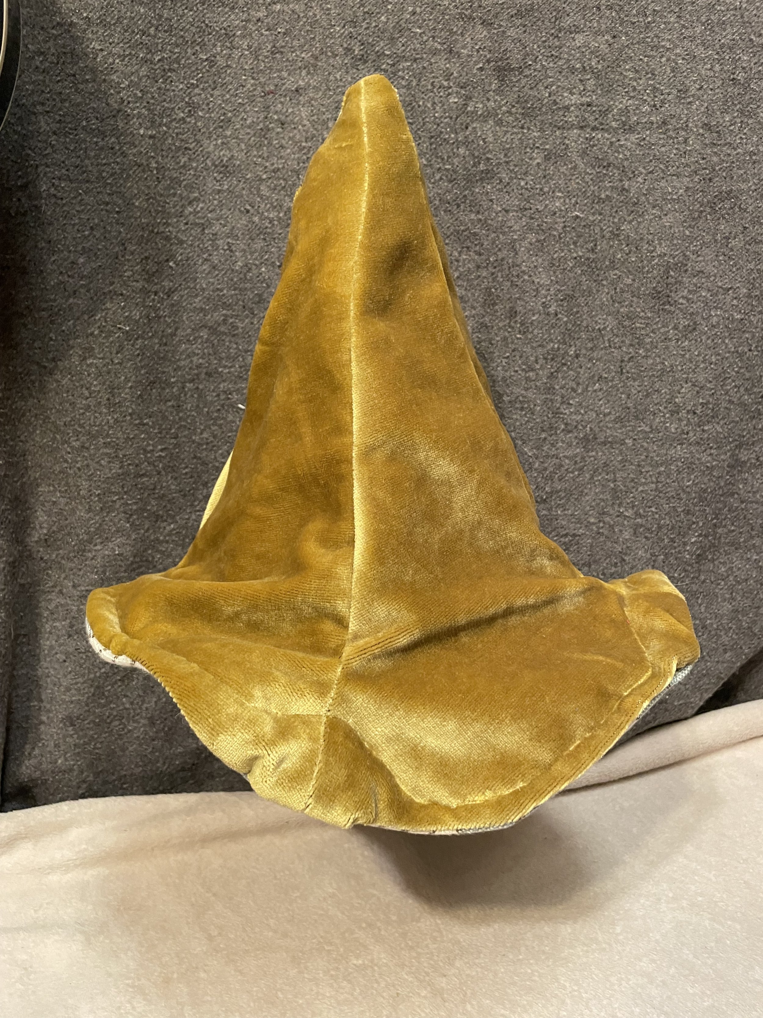 A piece of gold-colored velvet fabric folded into a cone shape, placed on a dark surface.