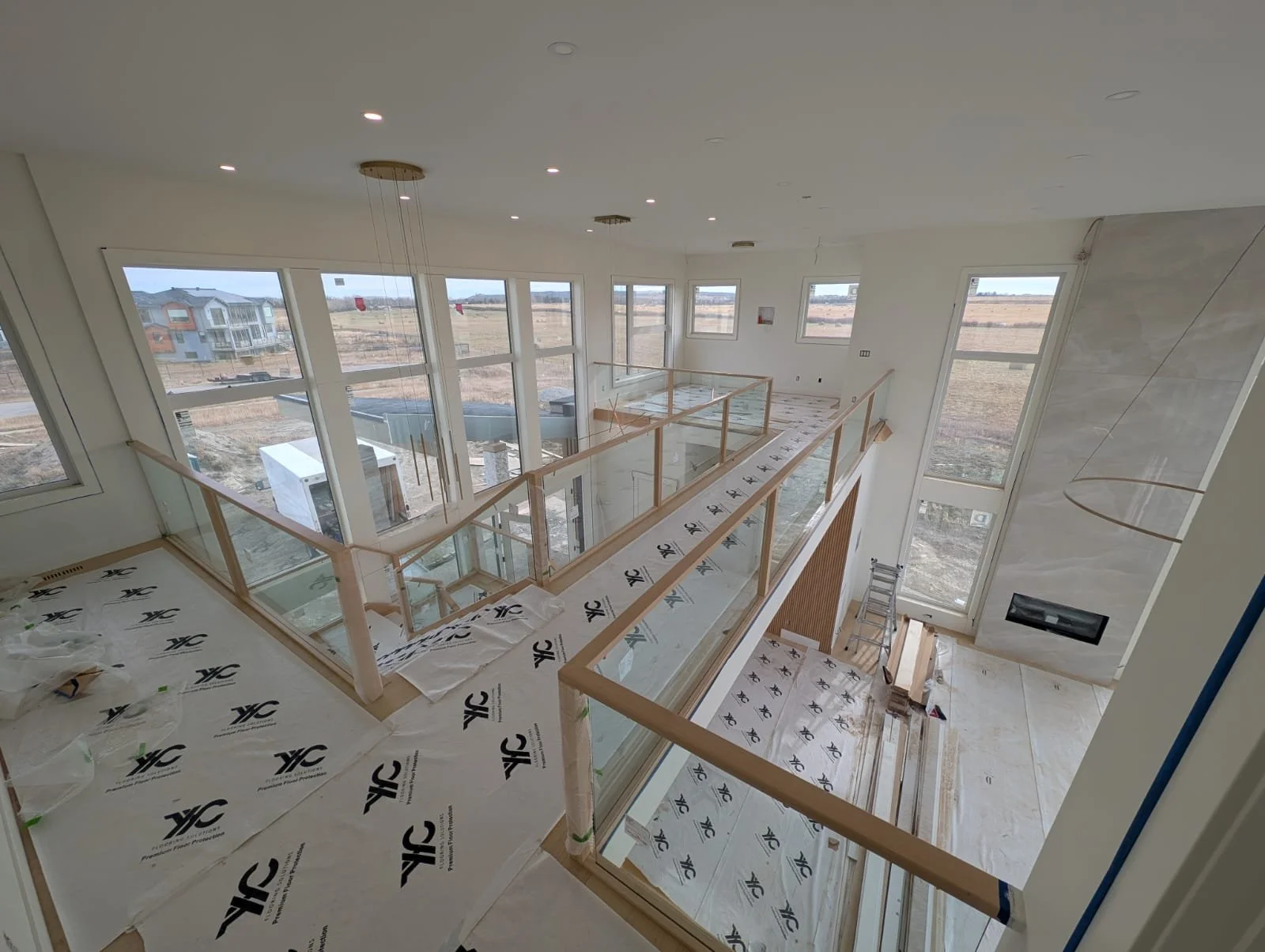 Interior of a two-story house under construction with large windows, glass railings, and ongoing finishing work.