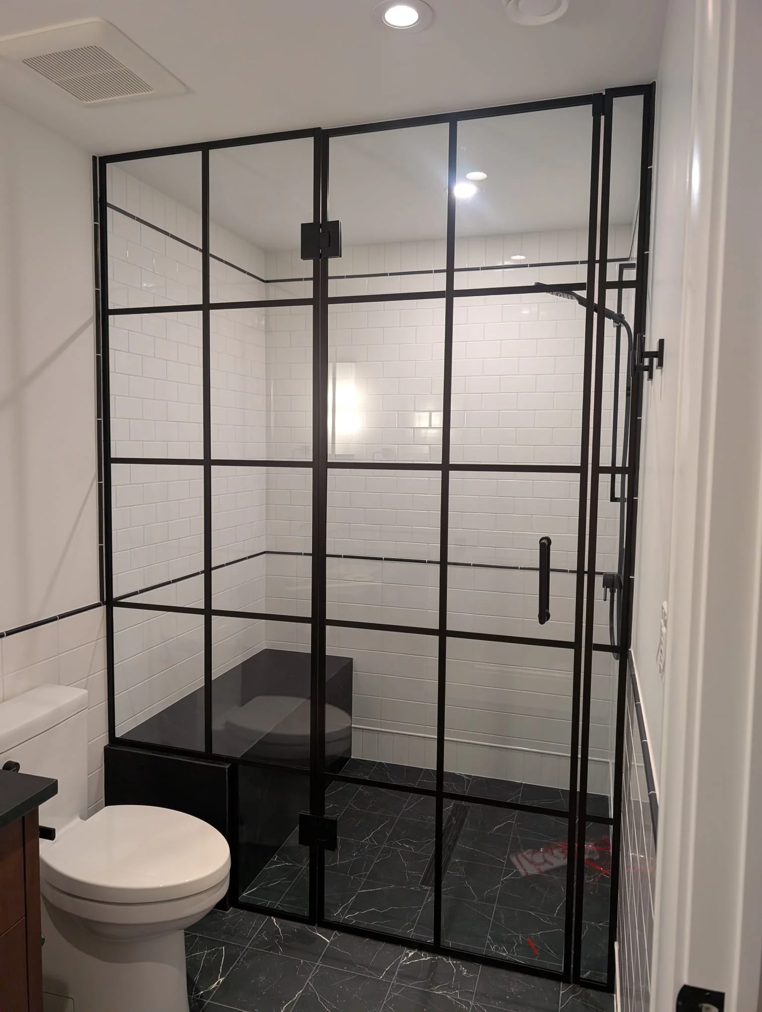 Modern bathroom with a glass shower enclosure, white subway tiles, black fixtures, and a black vanity with a marble floor.