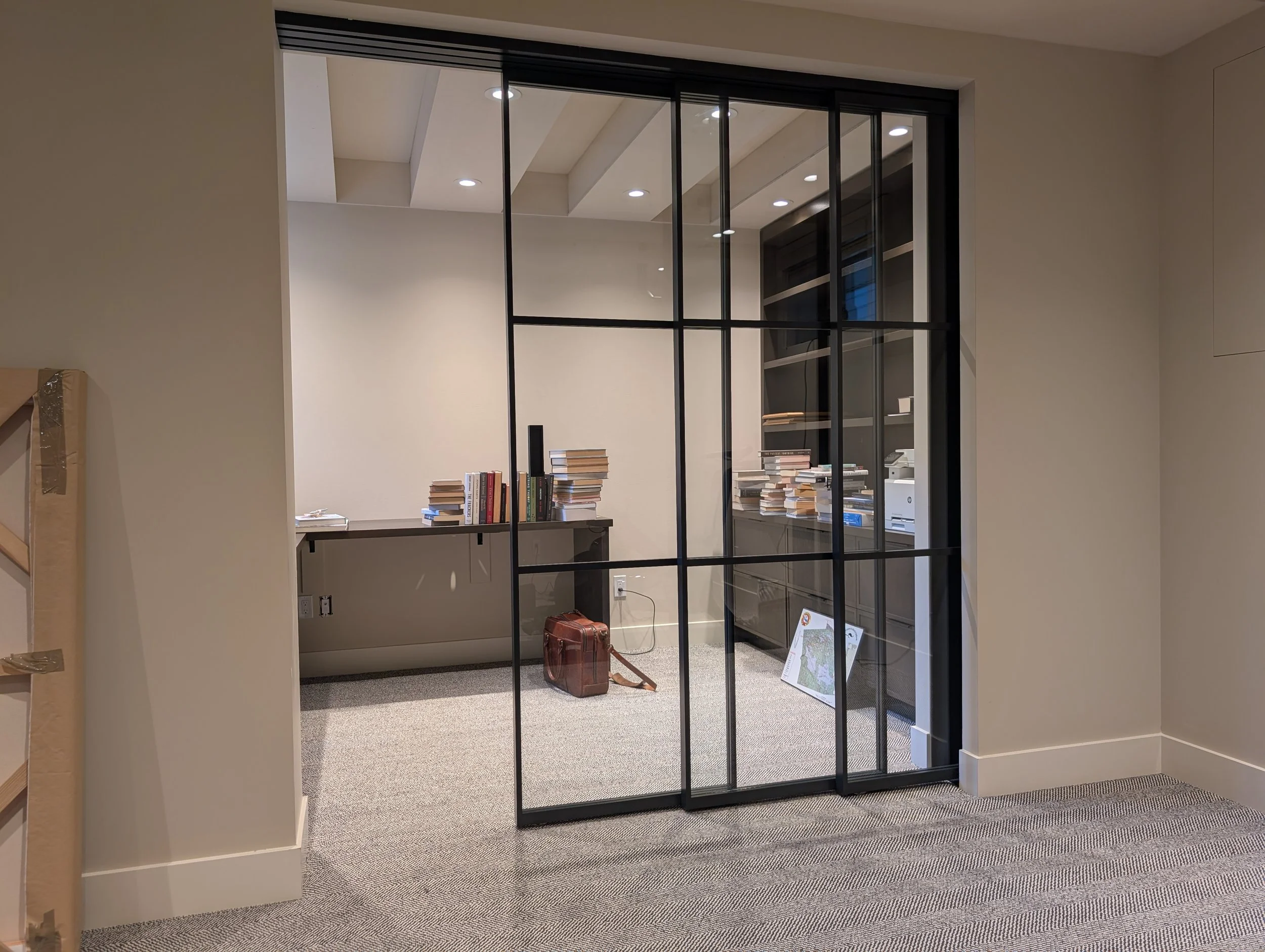 Office space with a glass partition, books, a suitcase, and electronic equipment