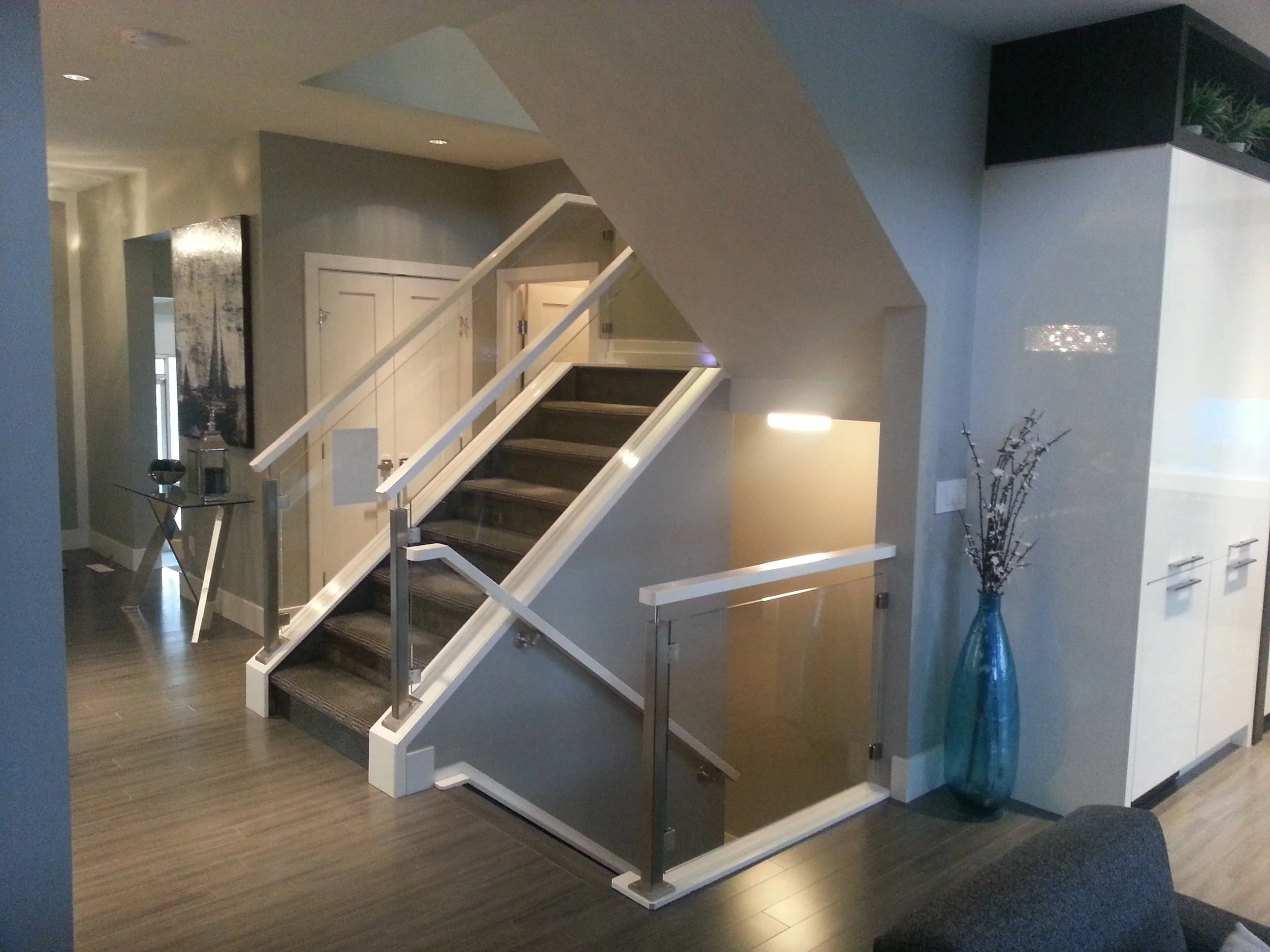 Interior of a modern home with a staircase leading to the upper floor, a tall blue vase with decorative branches, a white cabinet, and a small side table with decorations.
