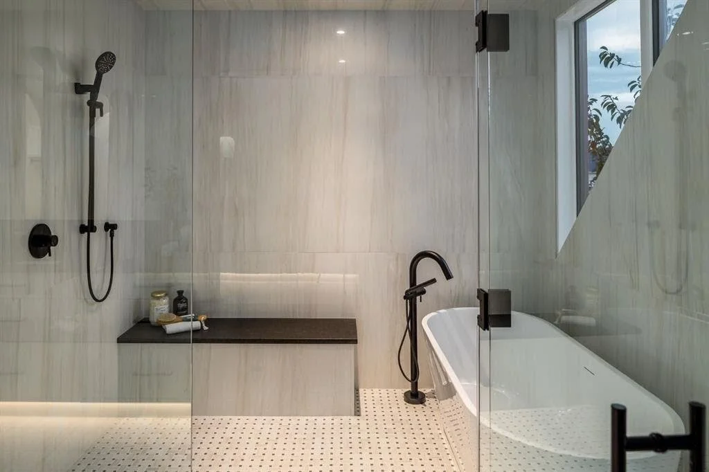 Modern bathroom featuring a walk-in shower with black fixtures and a bench, and a bathtub with black fixtures, glass enclosure, and a window with a partial view of trees outside.