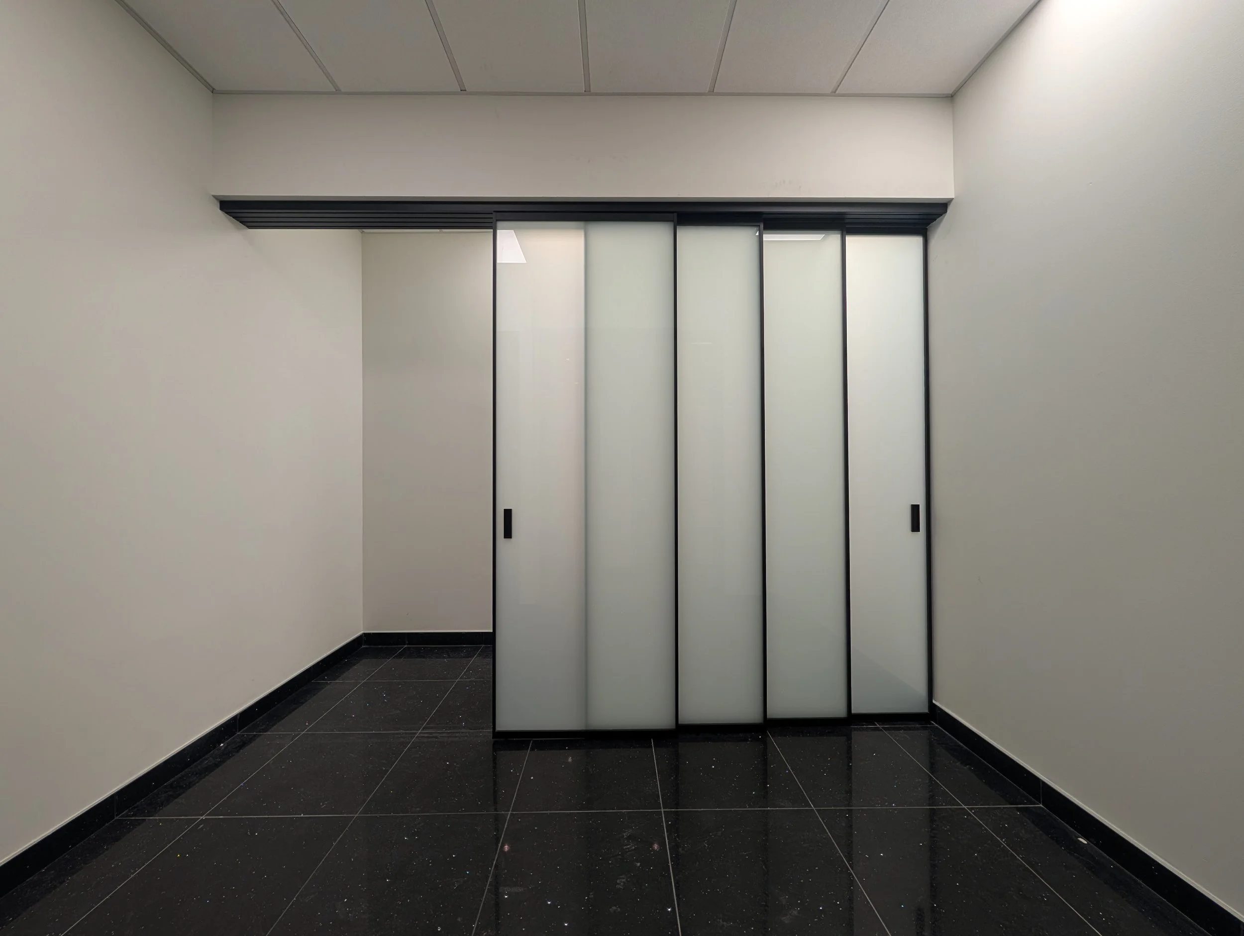 Frosted glass synchronized sliding doors in a minimalistic interior with black tiled floor.