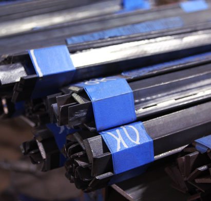 Bundles of black metal bars secured with blue tape, stacked together in a warehouse or storage area.