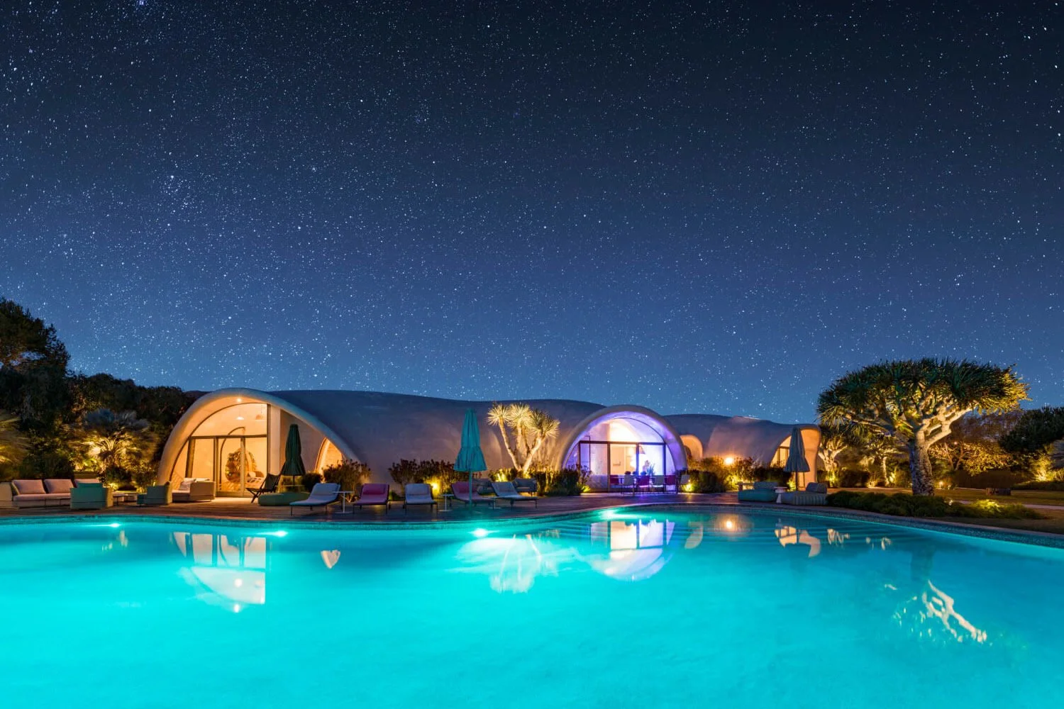Night view of a modern house with a swimming pool, illuminated outdoor seating, and starry sky.