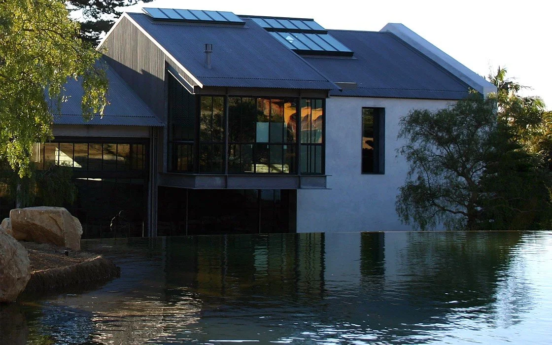 Modern house with large glass windows, metal roof, and a water feature in the foreground