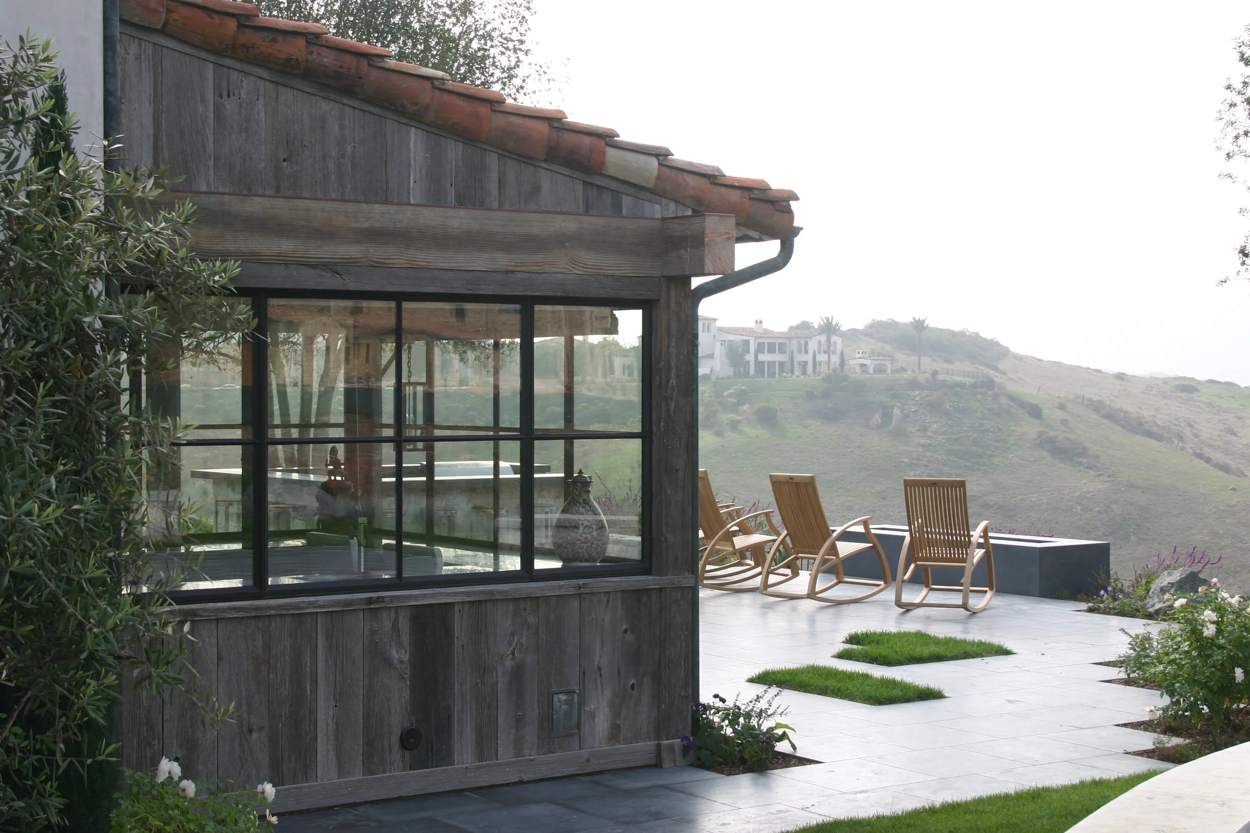 Outdoor patio with wooden chairs, small patches of grass, and a view of distant hillside homes.