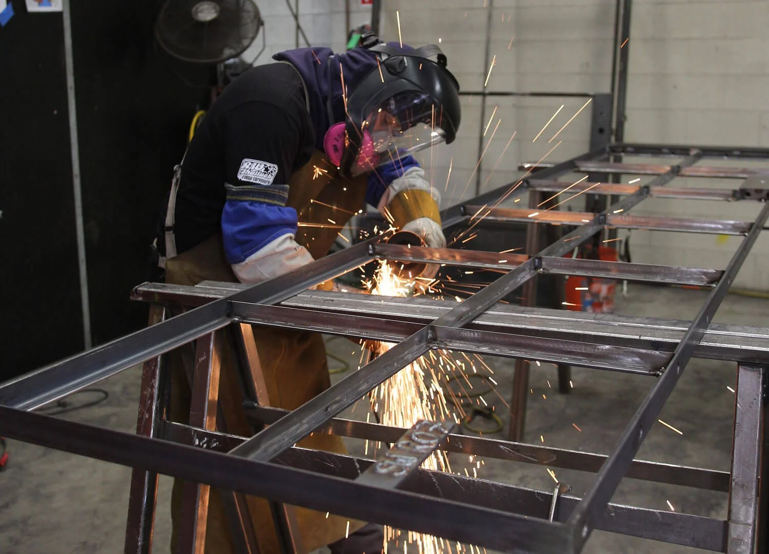 A person welding metal frame in a workshop with sparks flying.