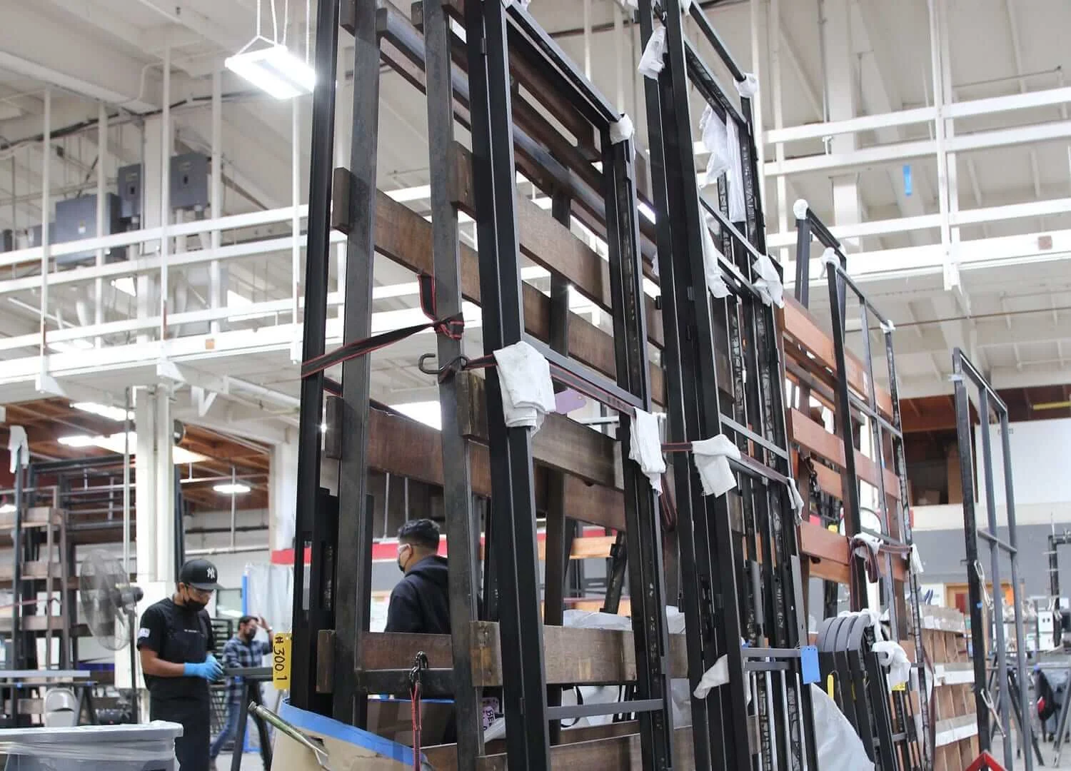 Large metal and wooden shelving units in a warehouse with two workers wearing masks and gloves.