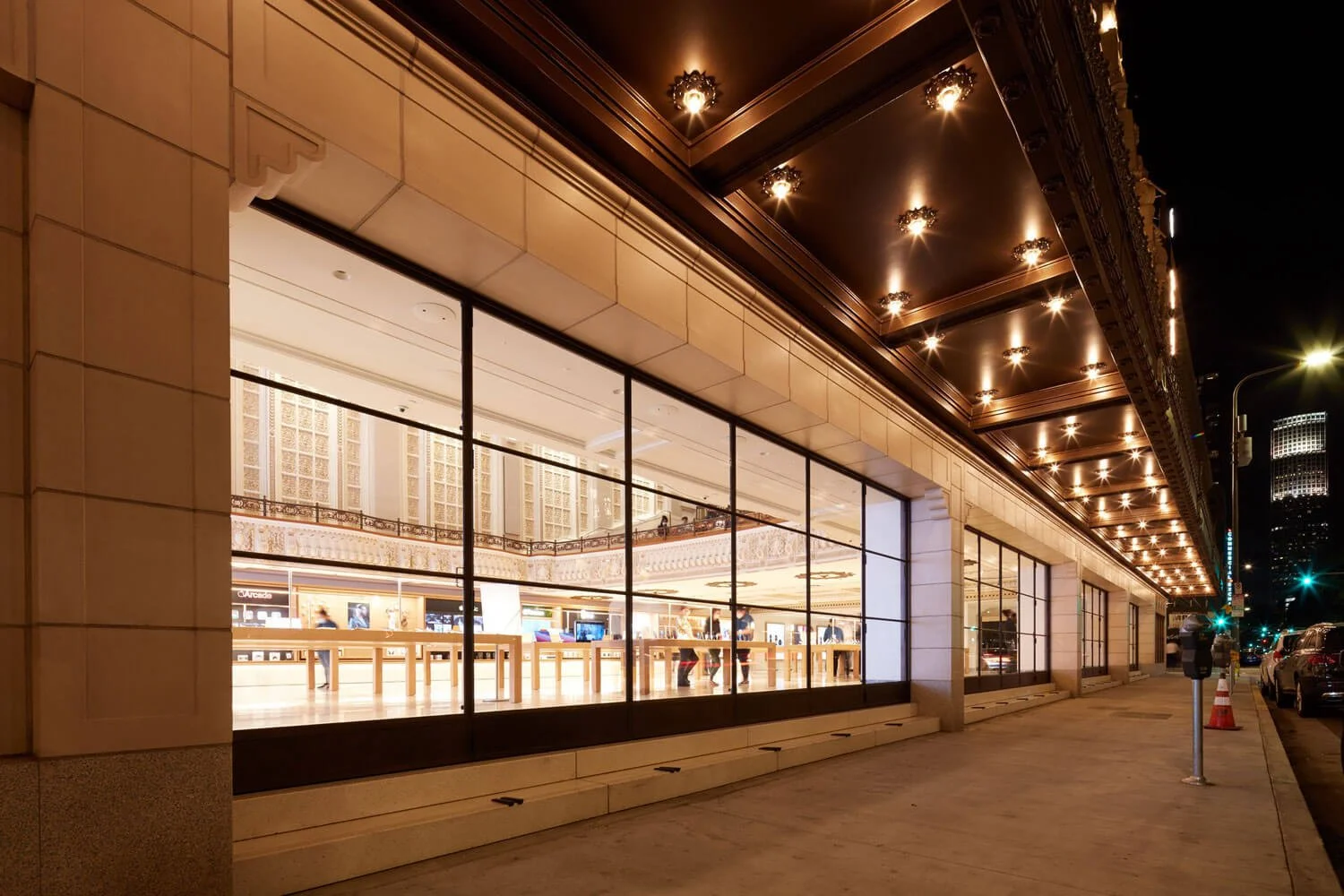 Night view of a commercial building with large glass windows displaying the brightly lit interior, and decorative lighting on the overhanging ceiling.