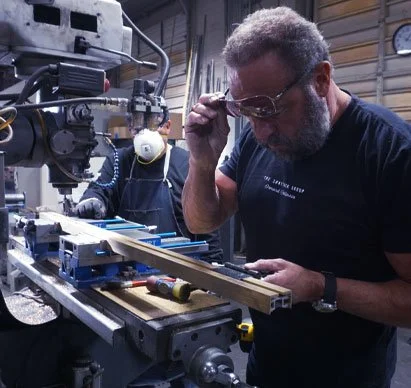 A man working with a milling machine in a workshop, wearing safety glasses and adjusting the machine.