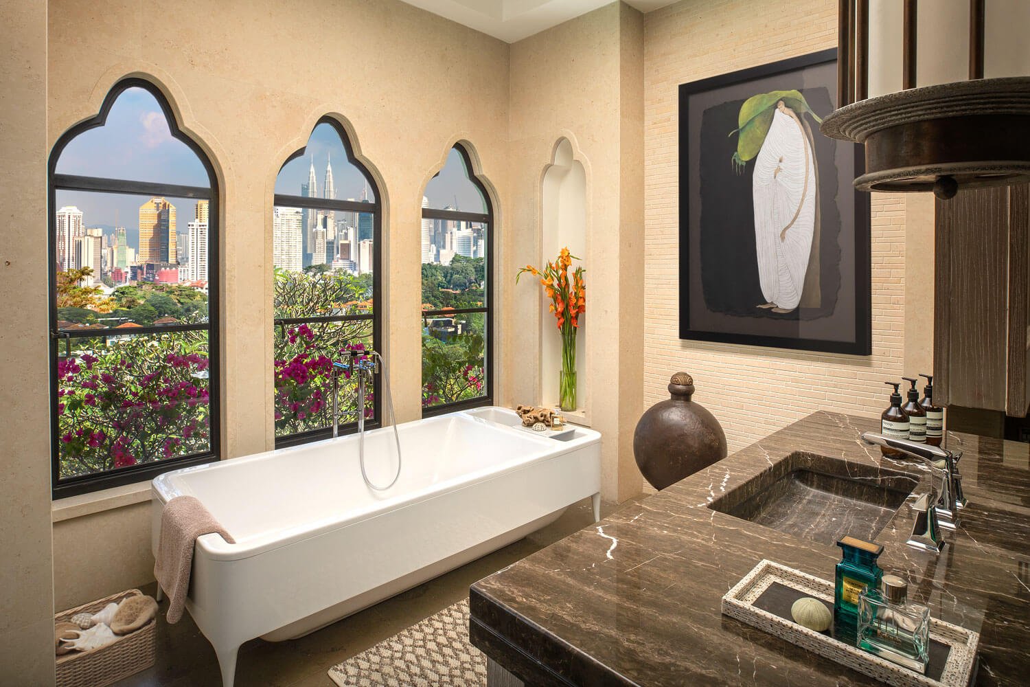 Interior of a luxurious bathroom with a bathtub, large windows with city views, a marble countertop with a sink, and modern decor including artwork and vases.
