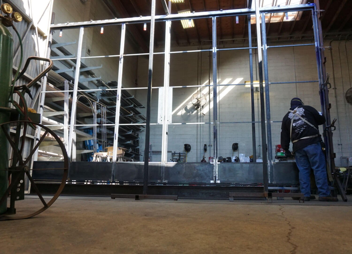 A person working on a large metal frame structure in a workshop or warehouse, with shelves and tools visible in the background.
