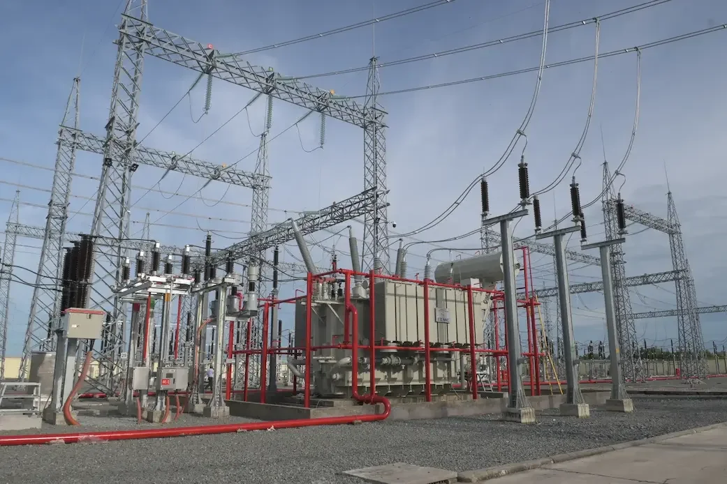 A large electrical substation featuring numerous wires and tall poles against a clear sky.