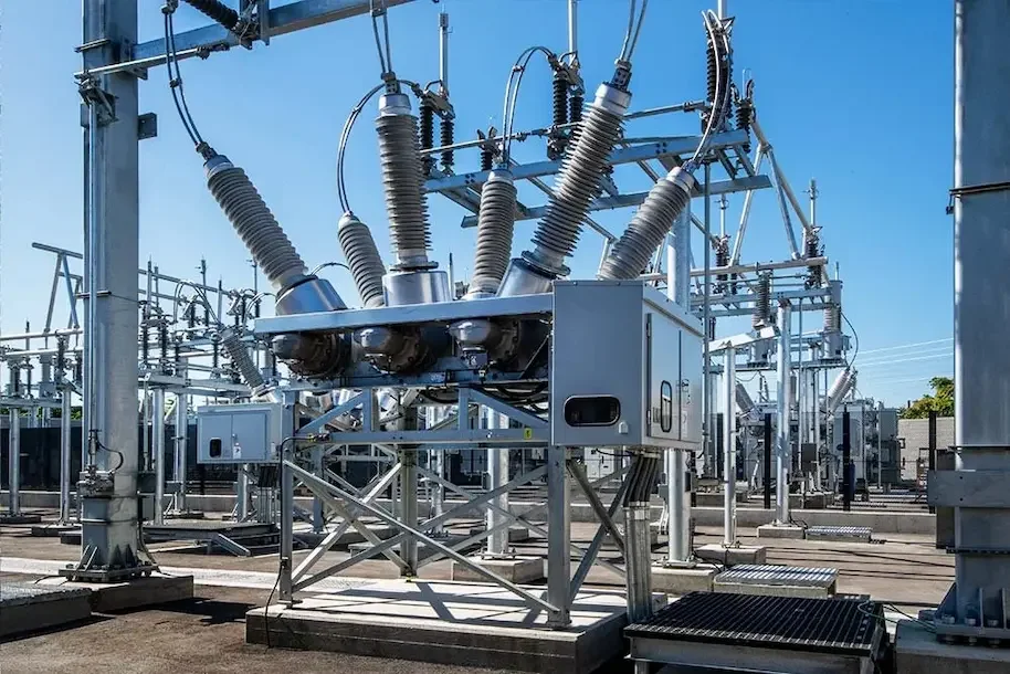 A large electrical substation featuring multiple large transformers and extensive power lines against a clear blue sky.