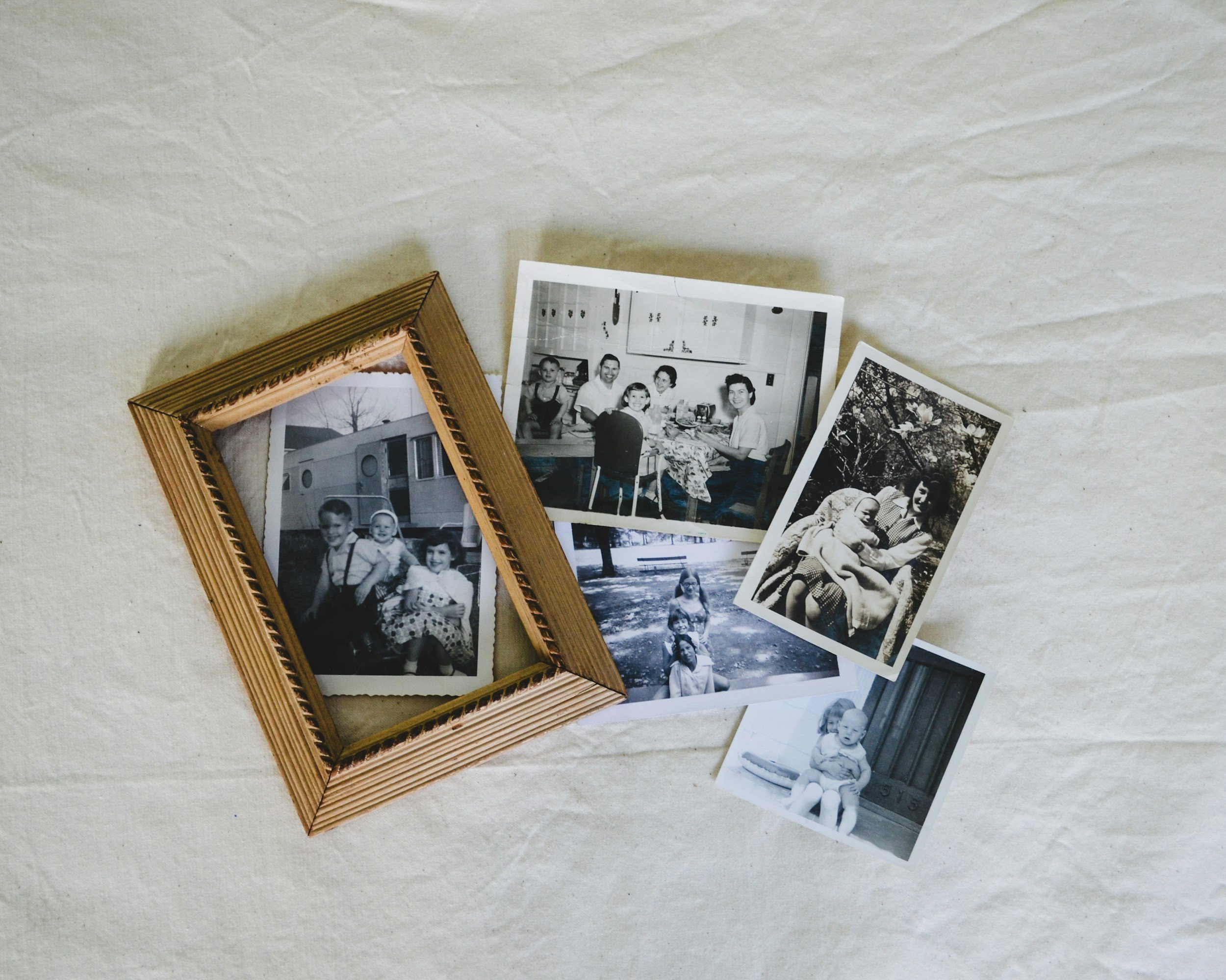 Collection of black and white family photographs laid out on a white surface, some in a wooden frame.