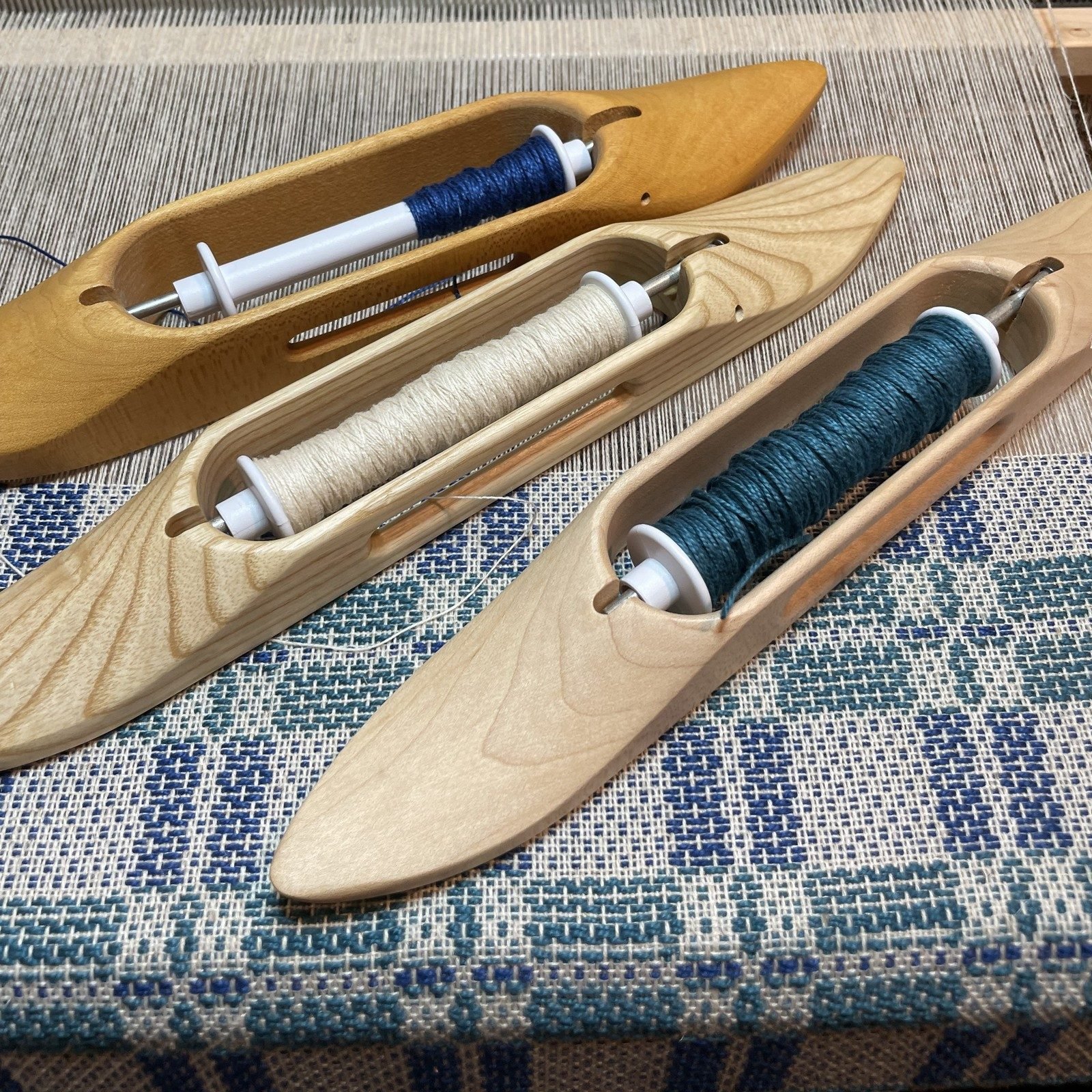 An Andrea White Designs woven table runner in process showing the three wooden shuttles used to make the fabric in the studio.