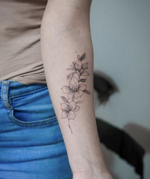 Close-up photograph of a fine line flower tattoo on forearm