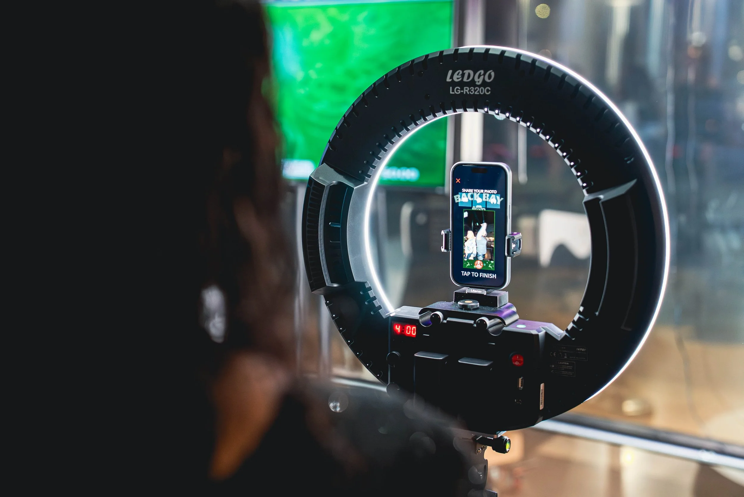 A smartphone mounted on a camera rig is capturing a photograph of a person doing a handstand. The scene is set indoors, with vibrant green and other colorful lights in the background.