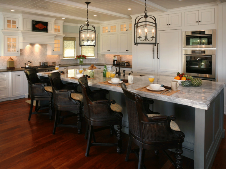 Bright kitchen with white cabinets, marble island countertop, dark wood flooring, black chandelier-style pendant lights, and breakfast setup with bowls, glasses, and fruit.