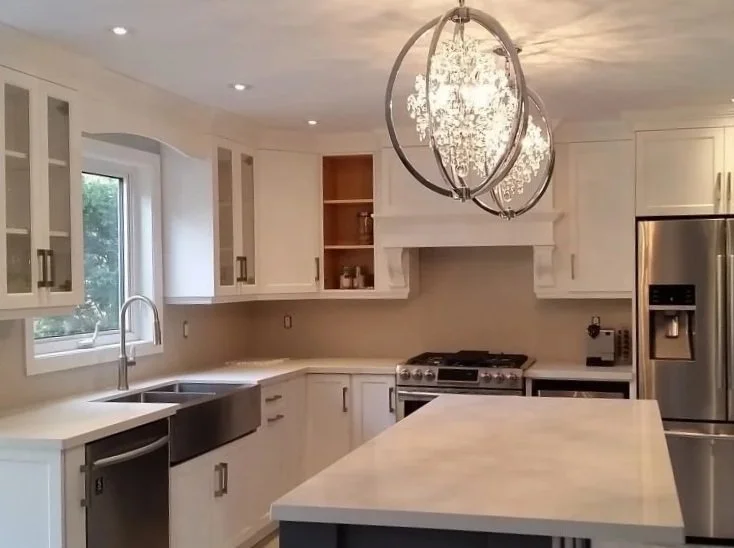 Modern kitchen with white cabinets, stainless steel appliances, a large beautiful countertop island, a window over the sink, and a chandelier lighting fixture.
