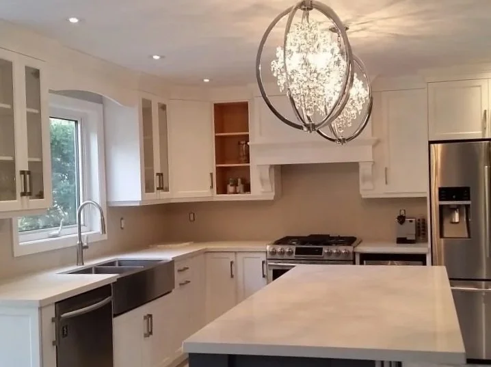 Modern kitchen with white cabinets, stainless steel refrigerator, black oven, and a large island with a white marble countertop illuminated by a contemporary chandelier.