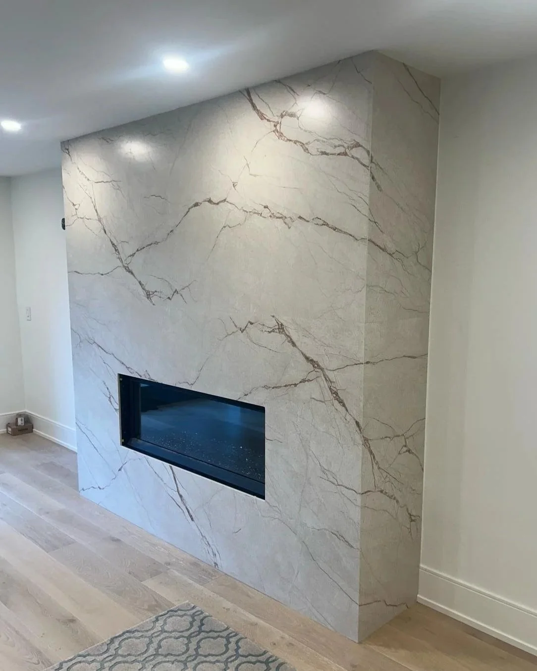 Large minimal porcelain fireplace surround in light cream colour and dark veining. 