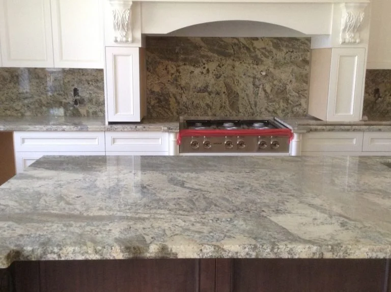 Kitchen with granite countertops, white cabinets, stainless steel stove, and a stone backsplash.