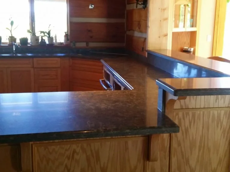 Kitchen counter with wooden cabinetry, potted plants on window sill, and a black granite countertop.