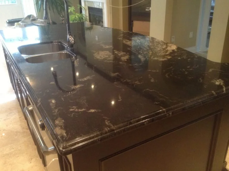 Kitchen island with a dark granite countertop, built-in sink, and a modern faucet in a well-lit kitchen.