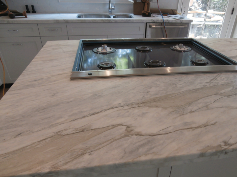 Kitchen countertop with a built-in gas cooktop, white cabinets, a sink, and a window with sunlight.